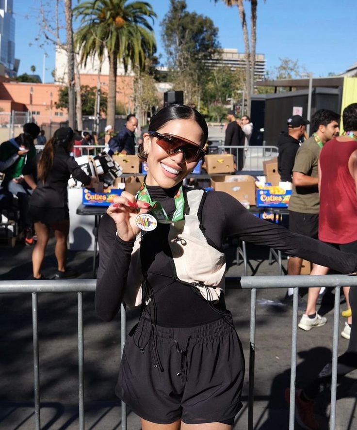 a woman standing next to a metal fence holding up a medal and wearing black shorts