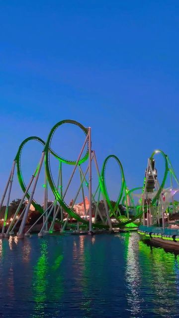 an amusement park with roller coasters in the water and lights reflecting on the water