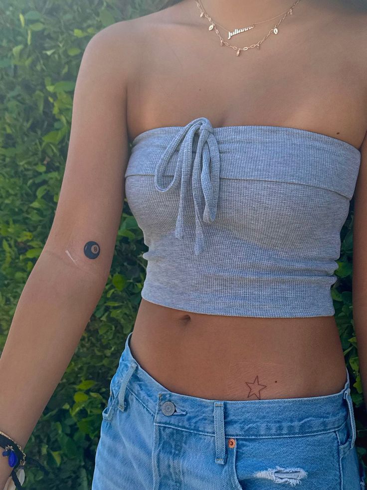 a woman with a small tattoo on her left arm, wearing blue jeans and a crop top