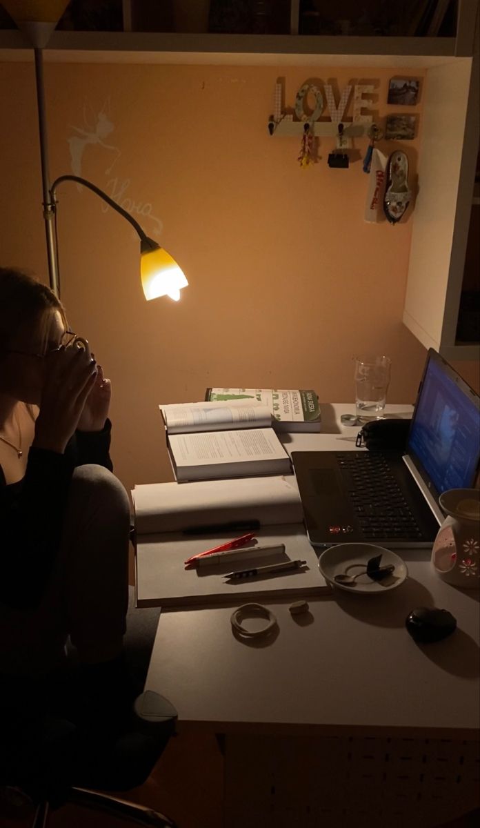 a woman sitting in front of a laptop computer on top of a desk next to a lamp