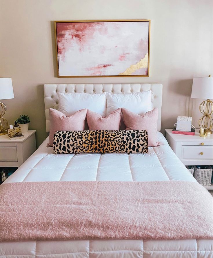 a white bed topped with pink pillows next to two nightstands and a painting on the wall