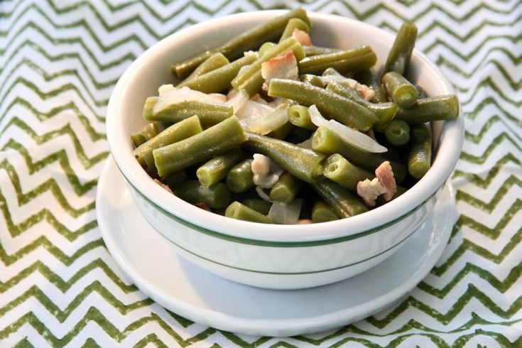 a white bowl filled with green beans on top of a striped table cloth next to a fork