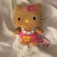 a hello kitty stuffed animal with a pink shirt and flowered skirt sitting on a white sheet