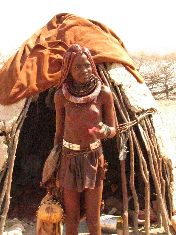 an african woman standing in front of her hut