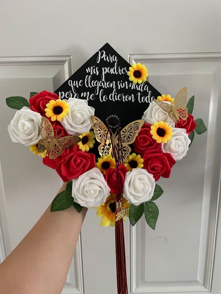 a hand holding a graduation cap with flowers and butterflies on it, in front of a door