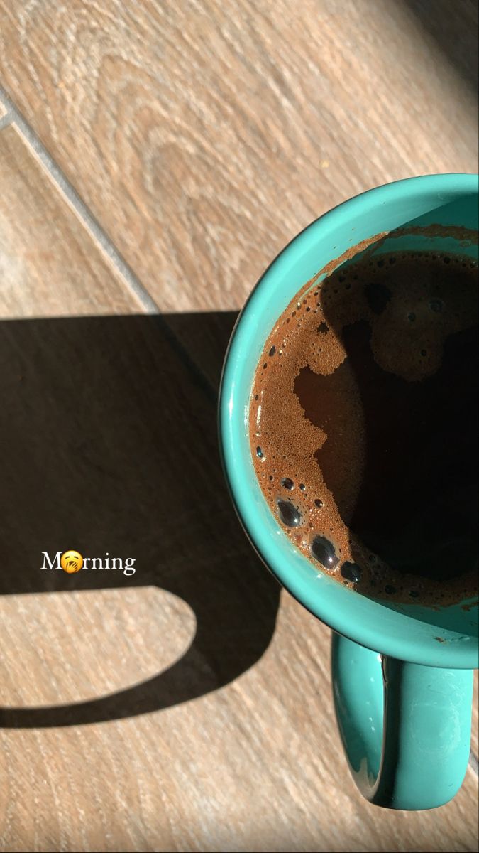 a cup of coffee sitting on top of a wooden table next to the shadow of a person's hand