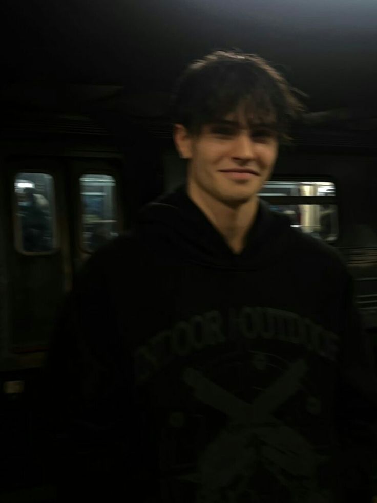 a young man in a black hoodie standing next to a subway car at night