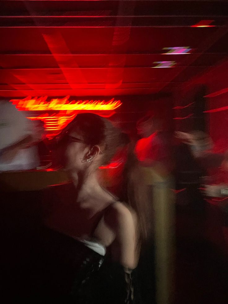 a blurry photo of people dancing in a dark room with red lights on the ceiling