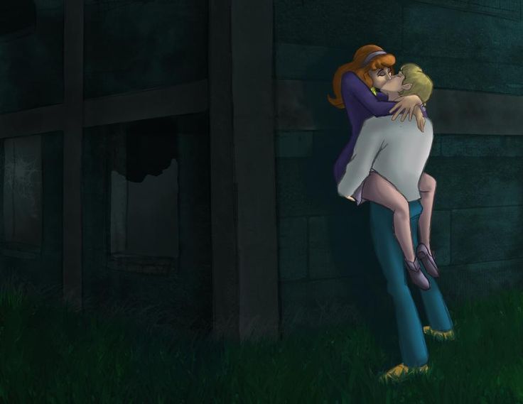 two people hugging each other in front of a brick building at night with green grass