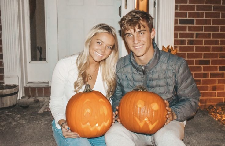 a man and woman sitting on the front steps holding pumpkins with faces carved into them