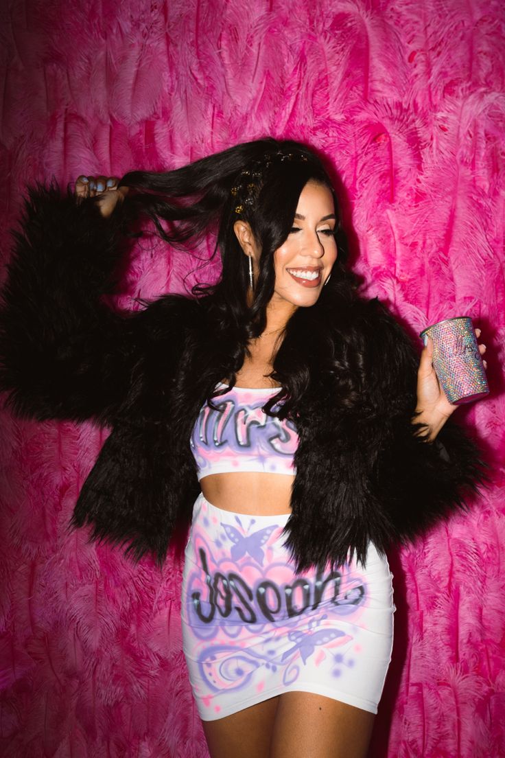 a woman posing in front of a pink wall