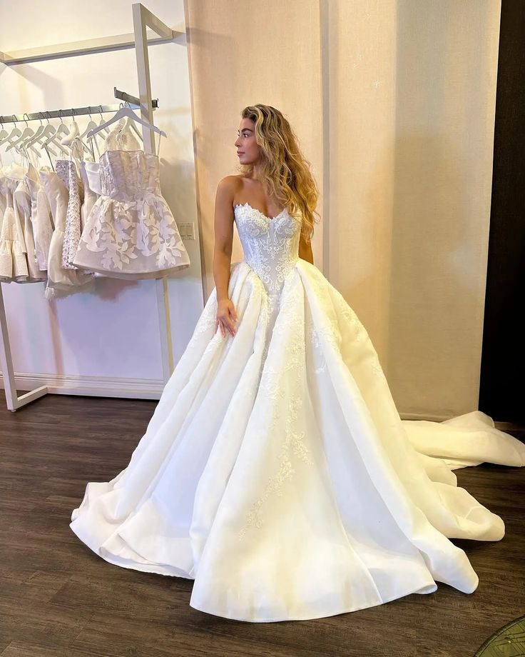 a woman in a white wedding dress standing next to a rack with dresses on it