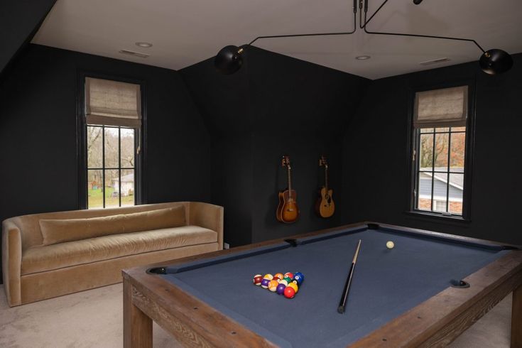 a pool table in the middle of a living room with two couches and guitars on the wall