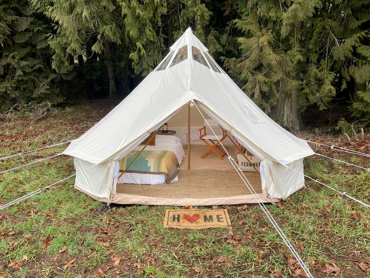 a tent set up in the middle of a forest with two beds and chairs inside