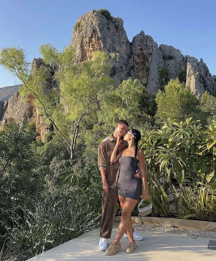 a man and woman standing next to each other in front of some mountains with trees