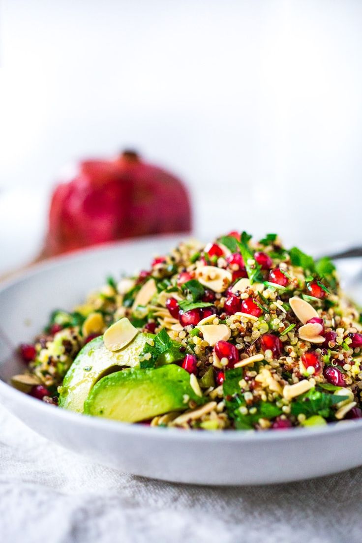 a white bowl filled with salad and topped with avocado, pomegranates