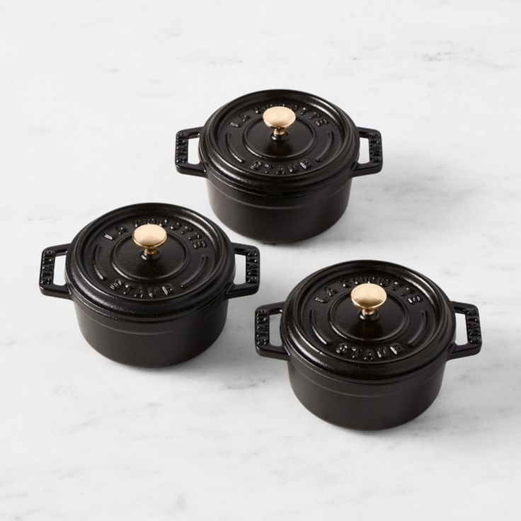 three black cast iron casserole dishes with gold knobs on the top and bottom