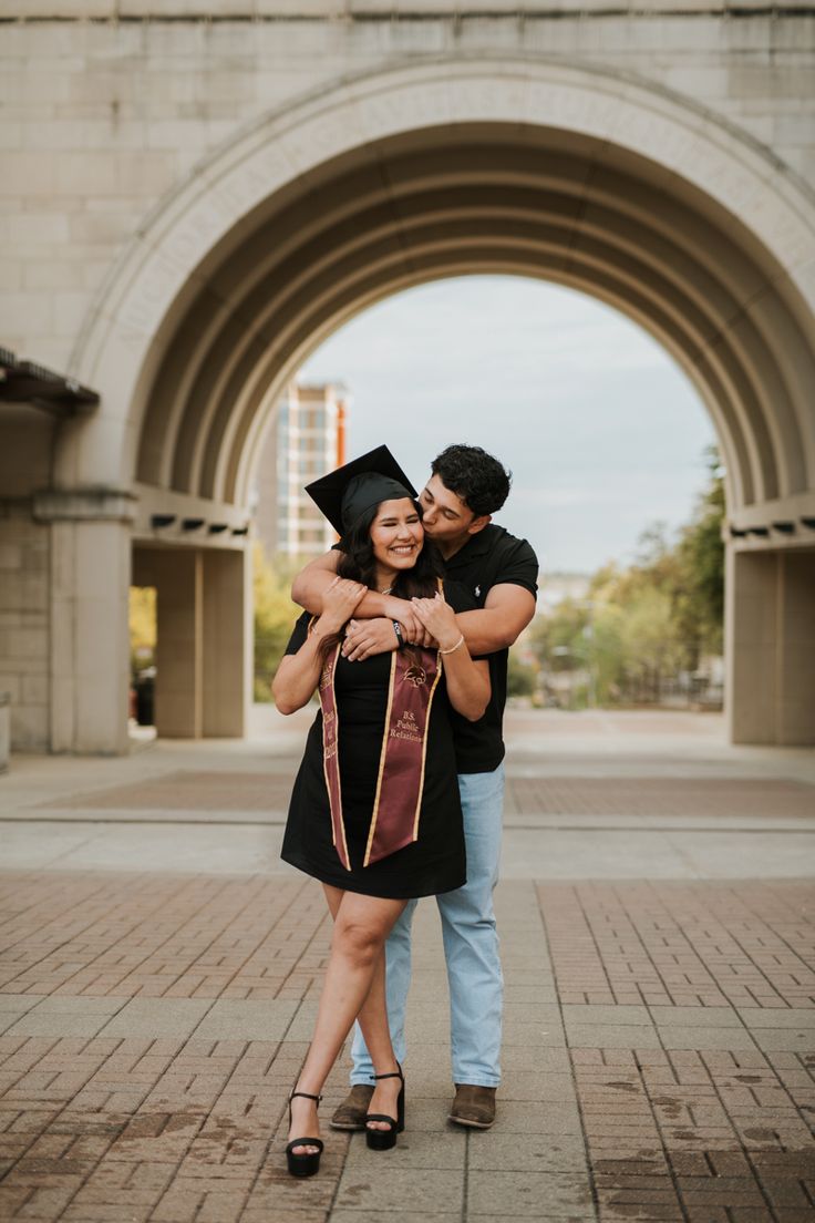 a man and woman hugging each other in front of an archway with a building in the background