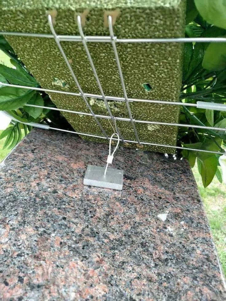 a piece of metal sitting on top of a granite counter next to green plants and bushes