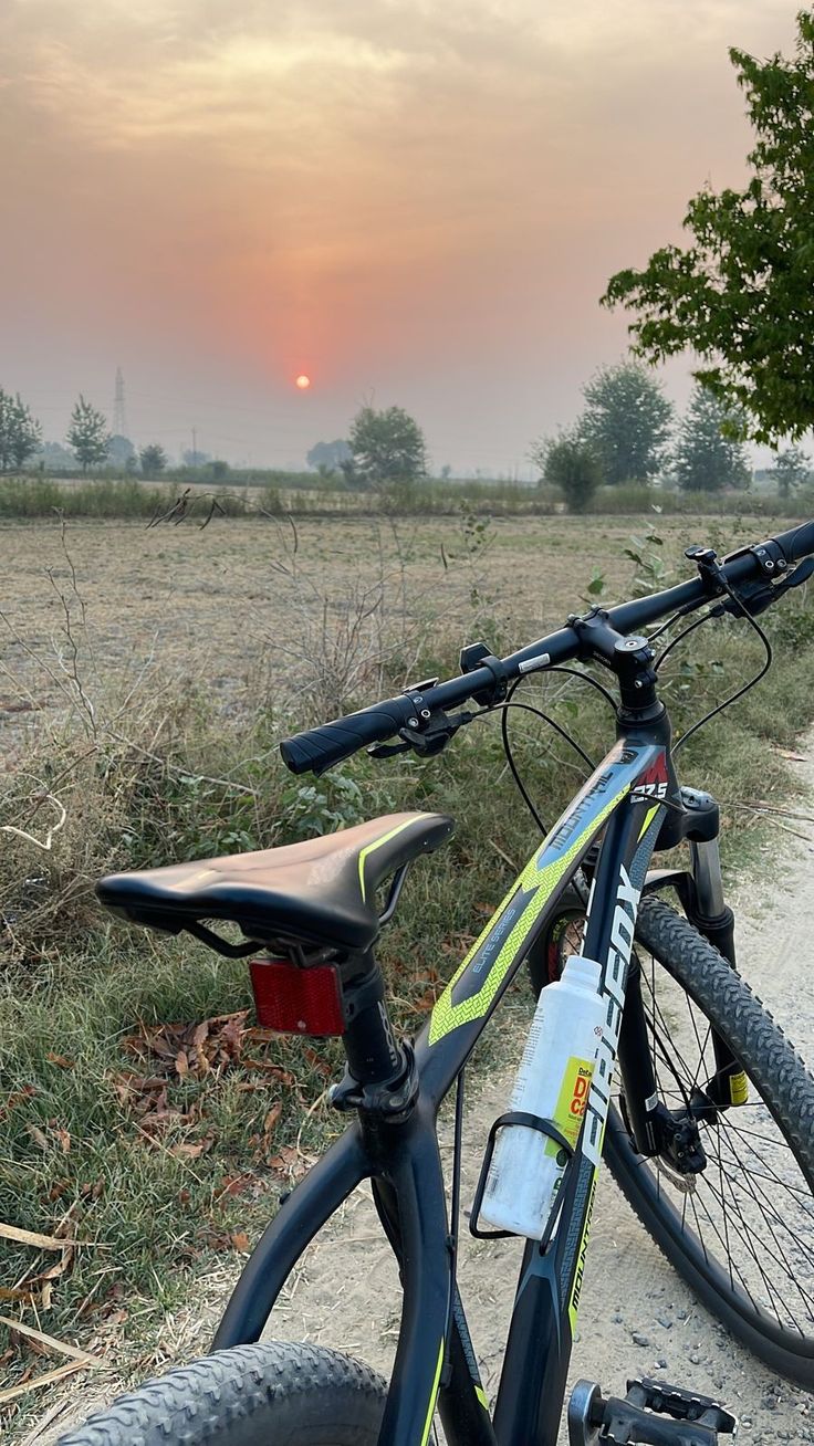 a bicycle parked on the side of a dirt road next to a grass covered field