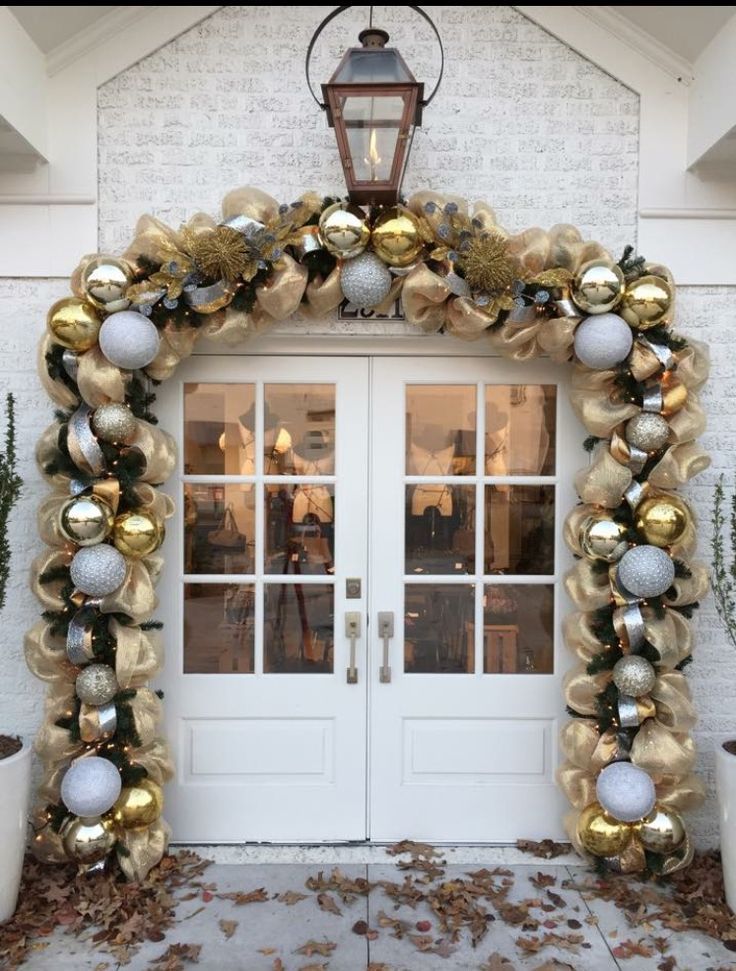 a white and gold arch with ornaments on the front entrance to a house that is decorated for christmas