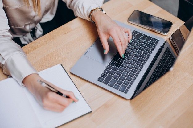 a woman sitting at a table with a laptop and cell phone in front of her