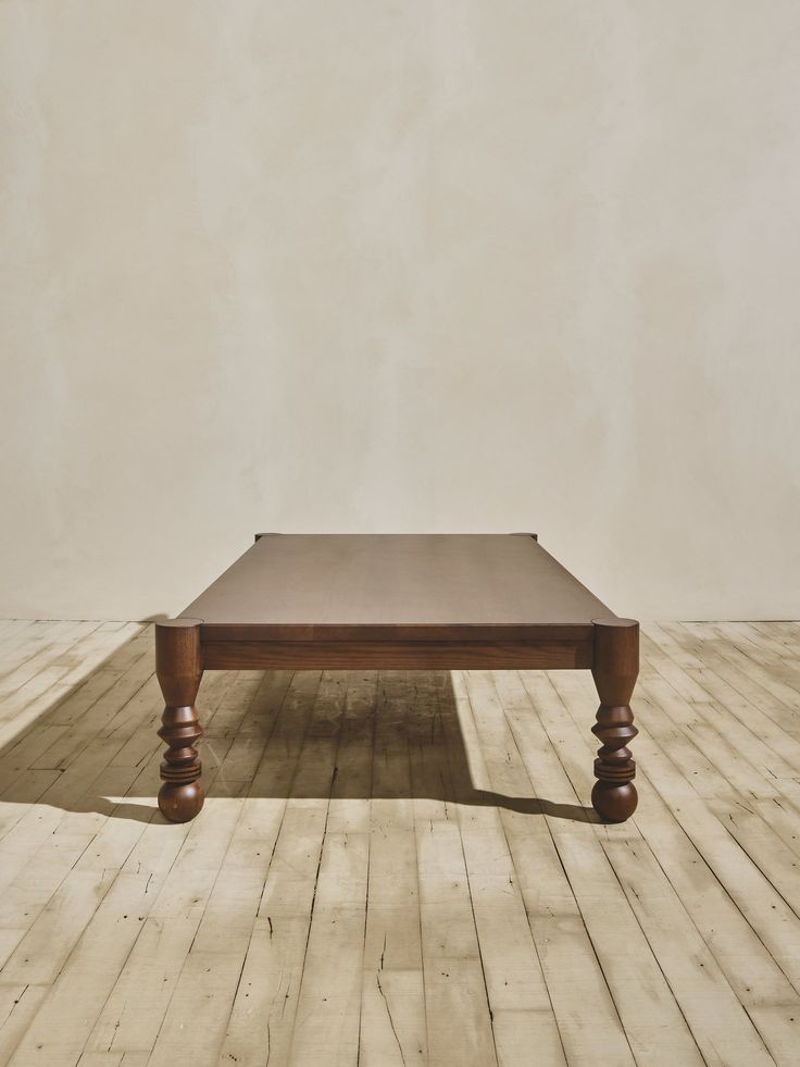 a wooden table sitting on top of a hard wood floor next to a white wall