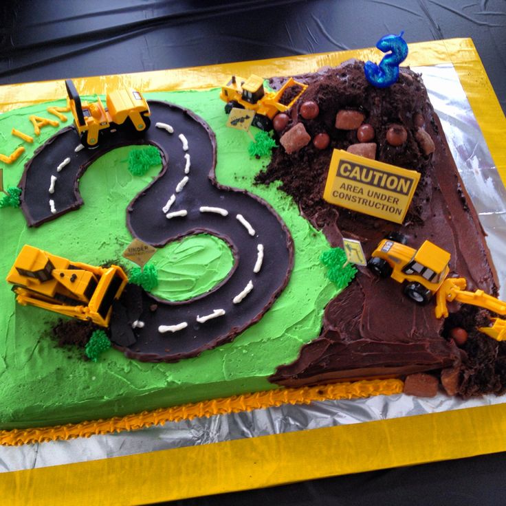 a birthday cake that is shaped like a road with construction vehicles on it and green frosting