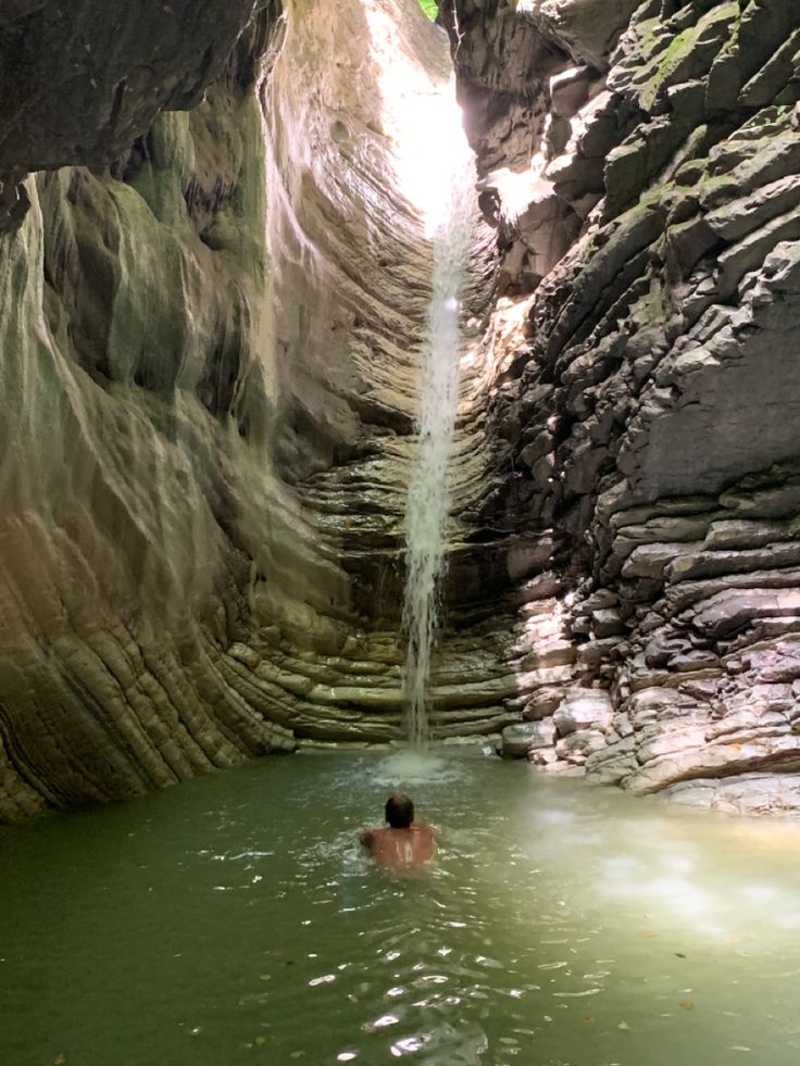 a man is swimming in the middle of a narrow pool with a waterfall coming out of it