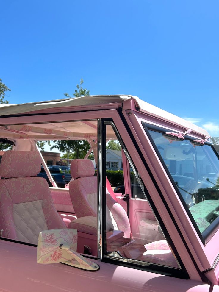 a pink car parked in a parking lot with its door open and the seat up