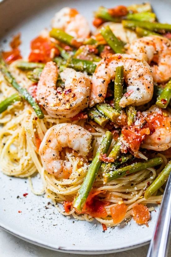 pasta with shrimp, asparagus and tomatoes on a white plate next to a fork