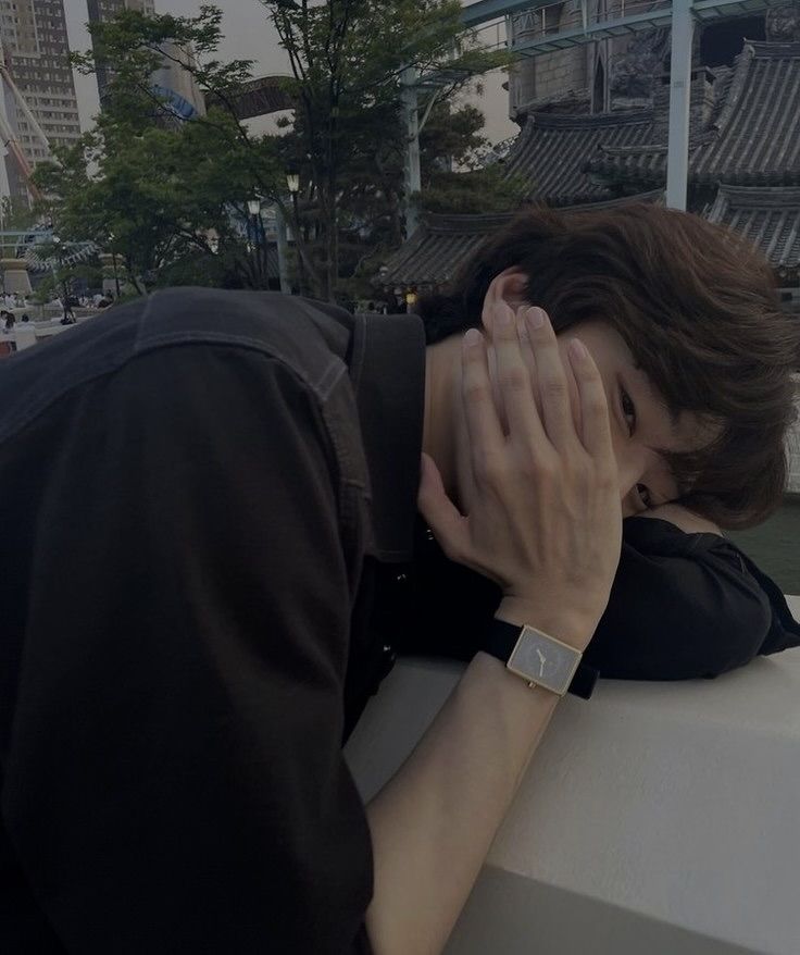 a woman covers her face with her hands as she leans against a wall in front of a cityscape