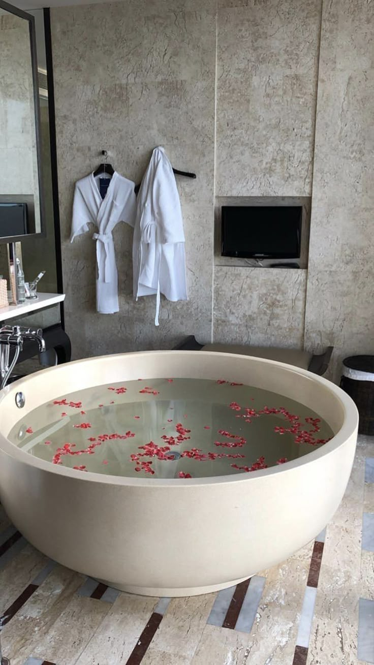 a large bath tub sitting inside of a bathroom next to a walk in shower with robes hanging on the wall