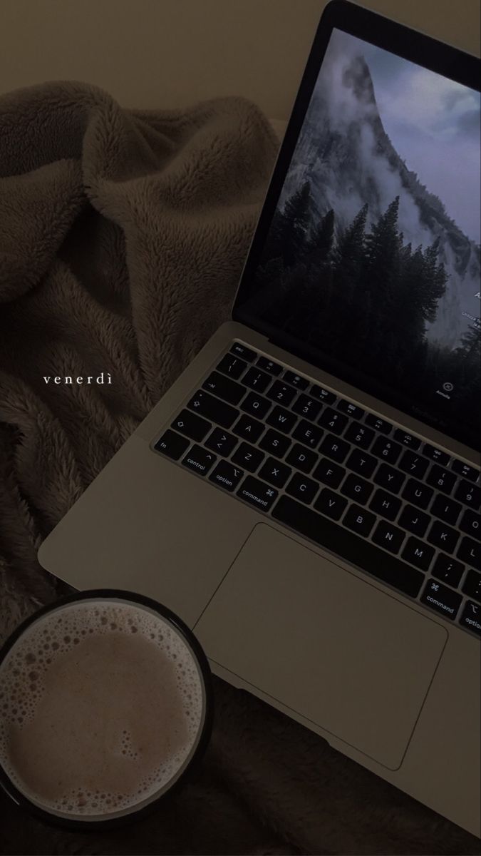 an open laptop computer sitting on top of a bed next to a cup of coffee