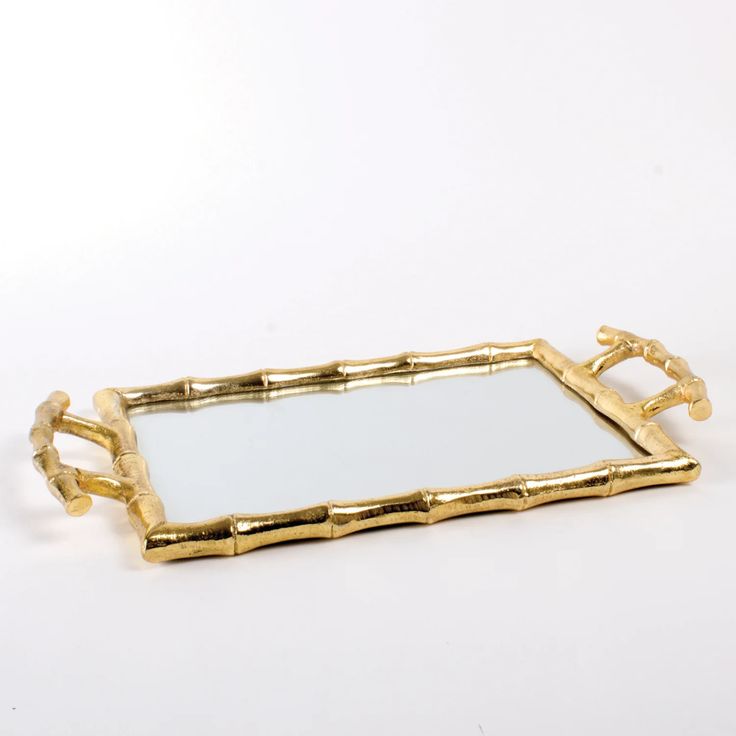 a gold bamboo tray with handles and mirror in the middle, on a white background