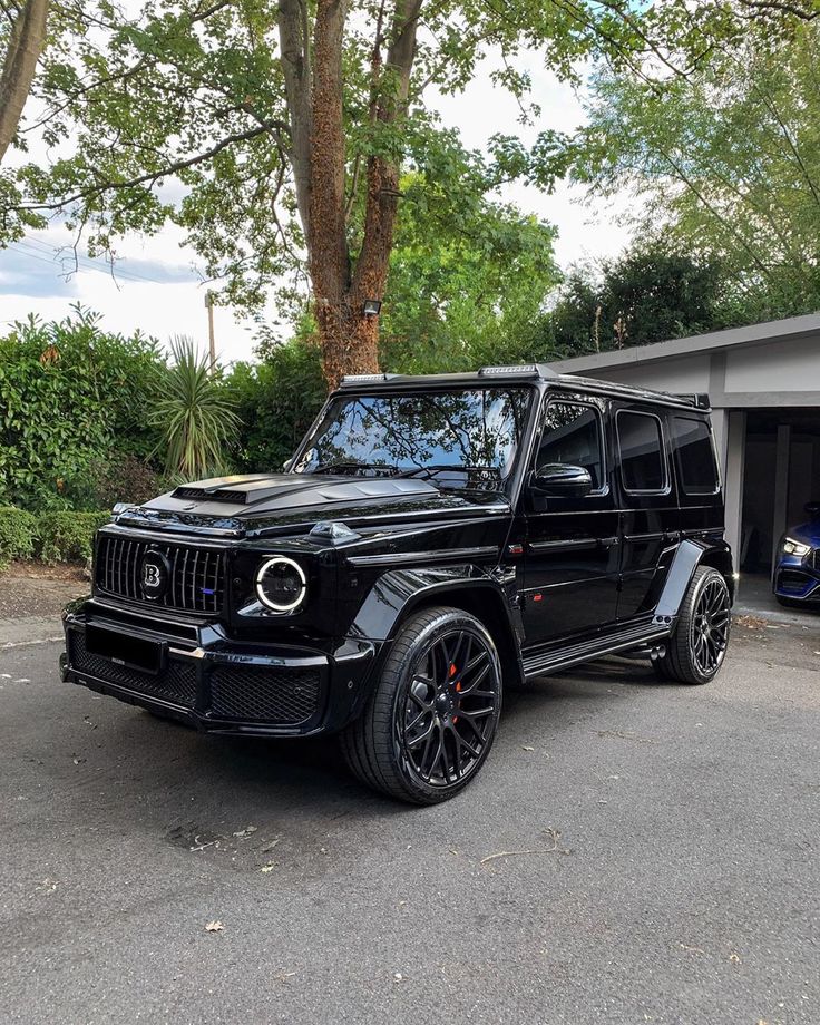 a black mercedes g - class is parked in front of a garage with its doors open