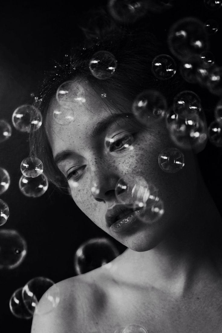 a woman is surrounded by soap bubbles in black and white photo, with her eyes closed