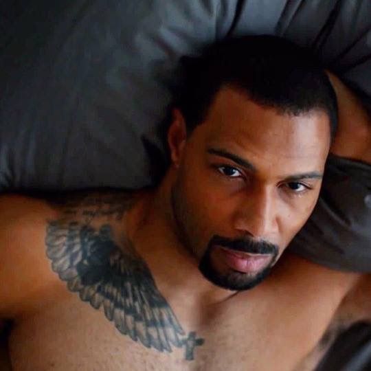 a shirtless man laying in bed with an eagle tattoo on his chest