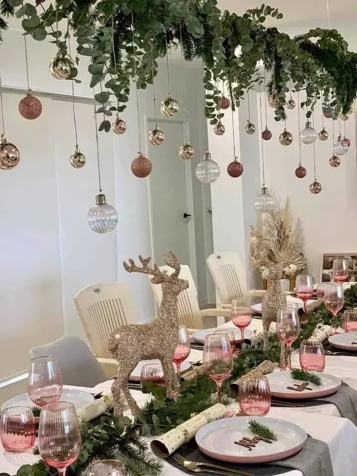 the table is set for christmas dinner with ornaments hanging from the ceiling and deer figurines