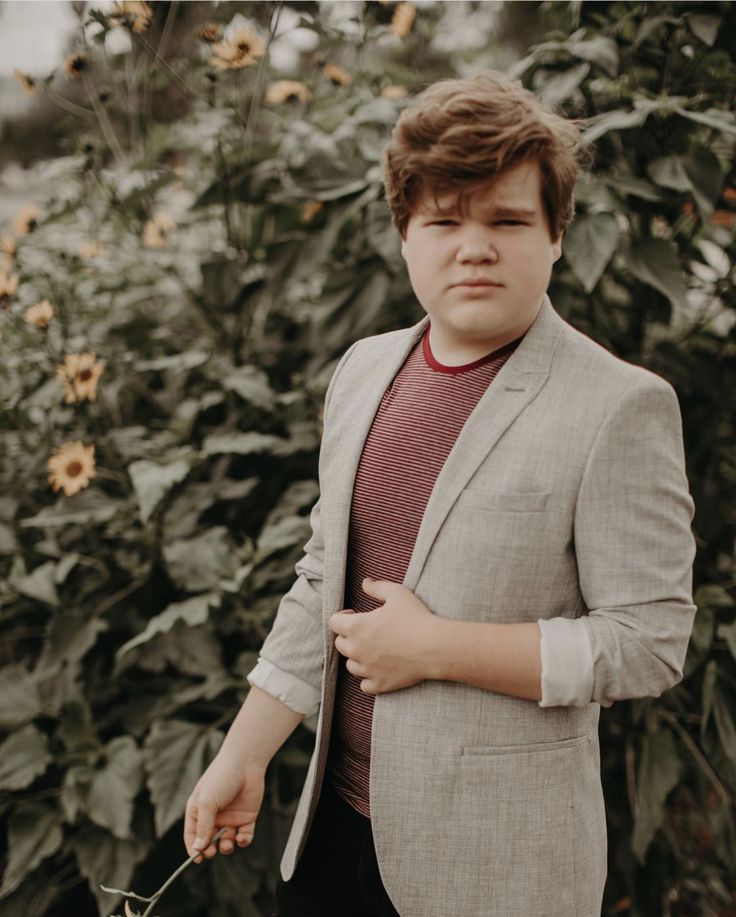 a young man in a suit and tie standing next to a bush with sunflowers