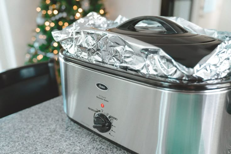 an aluminum foil wrapped crock pot sitting on top of a counter next to a christmas tree