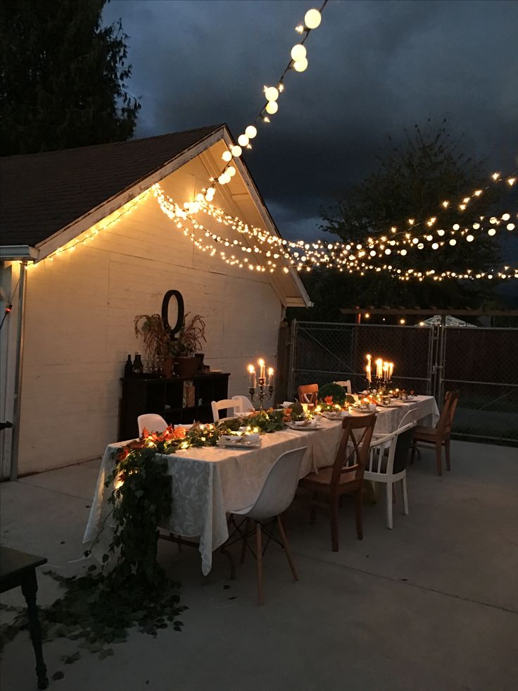 an outdoor dining table set up with candles and greenery on the table for dinner