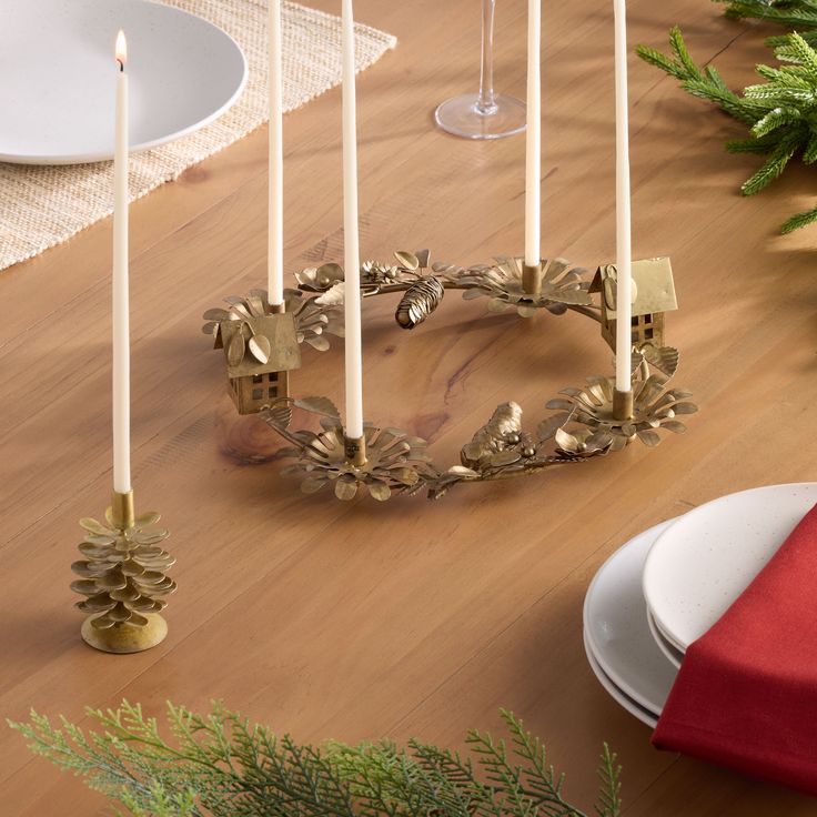 a table with candles, plates and napkins sitting on top of it next to a christmas tree