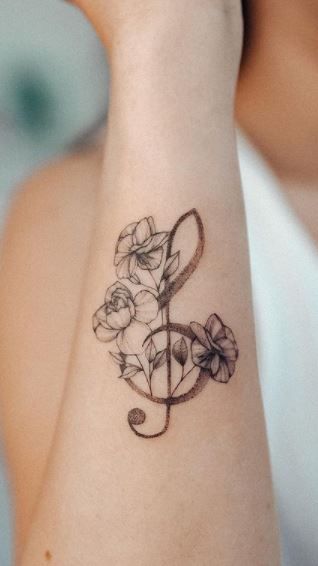 a woman's arm with a musical note and flowers tattoo on her left wrist