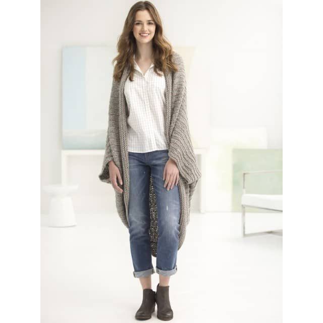 a woman standing in a white room wearing jeans and a cardigan sweater with an open front