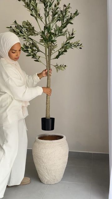 a woman in white holding a potted plant next to a large vase with a tree on it