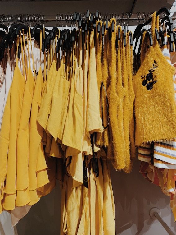 clothes hanging on racks in a store with yellow and brown colors, including black ones