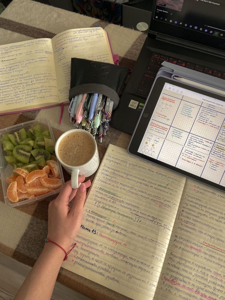 a person holding a cup of coffee in front of an open book and laptop computer