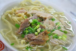 a white bowl filled with noodles and meat in broth next to a cup of soup