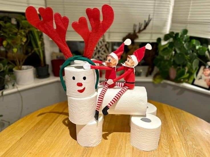 two elfs are sitting on top of toilet paper roll holders and one is holding a snowman